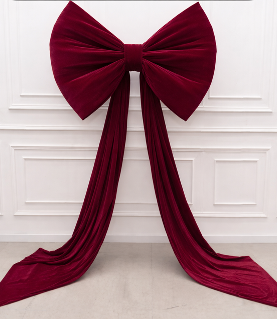Large burgundy bow with long ribbons against a white paneled wall.